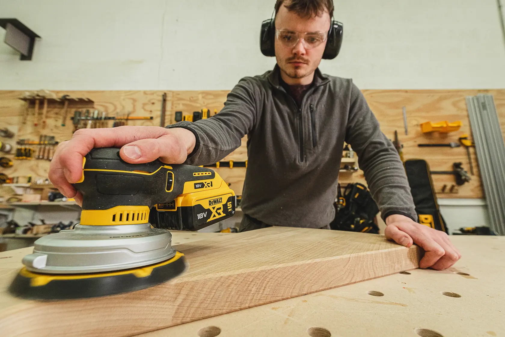 Personne ponçant du bois avec une ponceuse sans fil DEWALT DCW230N-XJ dans un atelier.