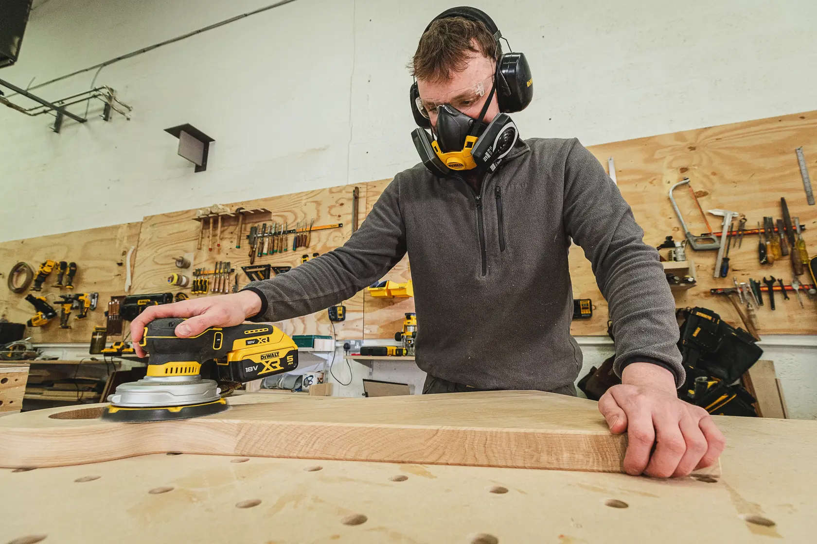 Personne ponçant du bois avec une ponceuse DEWALT, équipée de protections dans un atelier outillé.