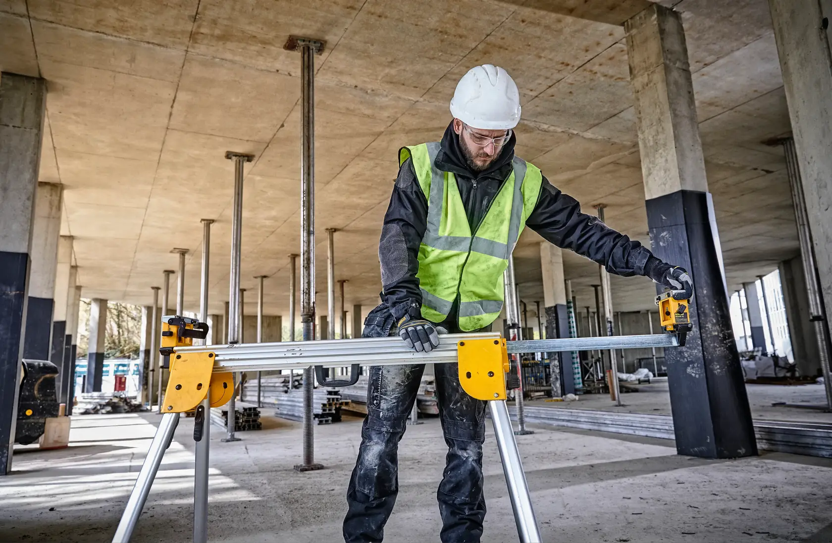 Ouvrier utilisant un support de scie DEWALT DE7033 sur un chantier, portant un équipement de sécurité, intérieur.