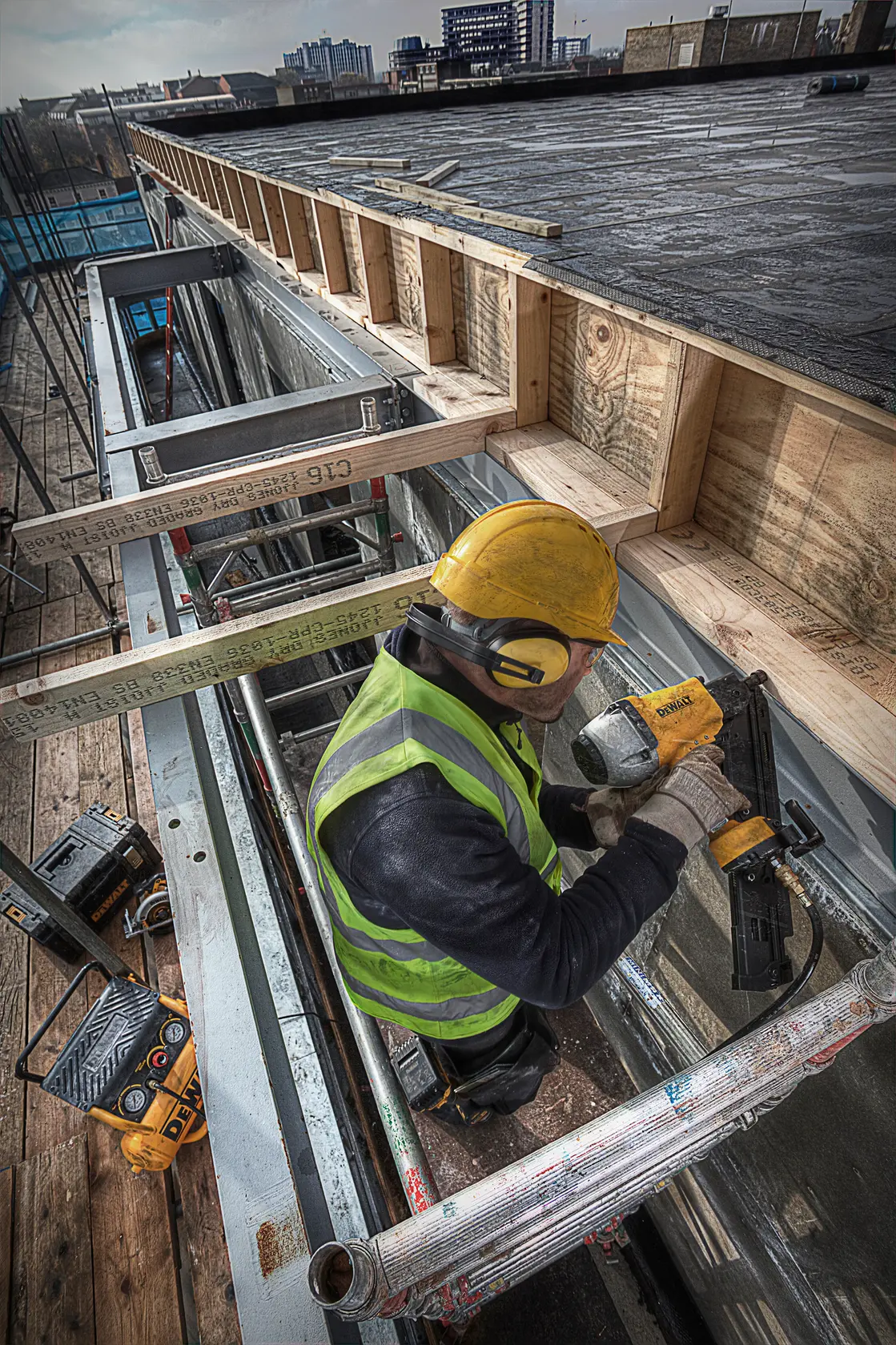 Ouvrier équipé utilise un pistolet à clous DEWALT sur un chantier avec cadre bois et métal.