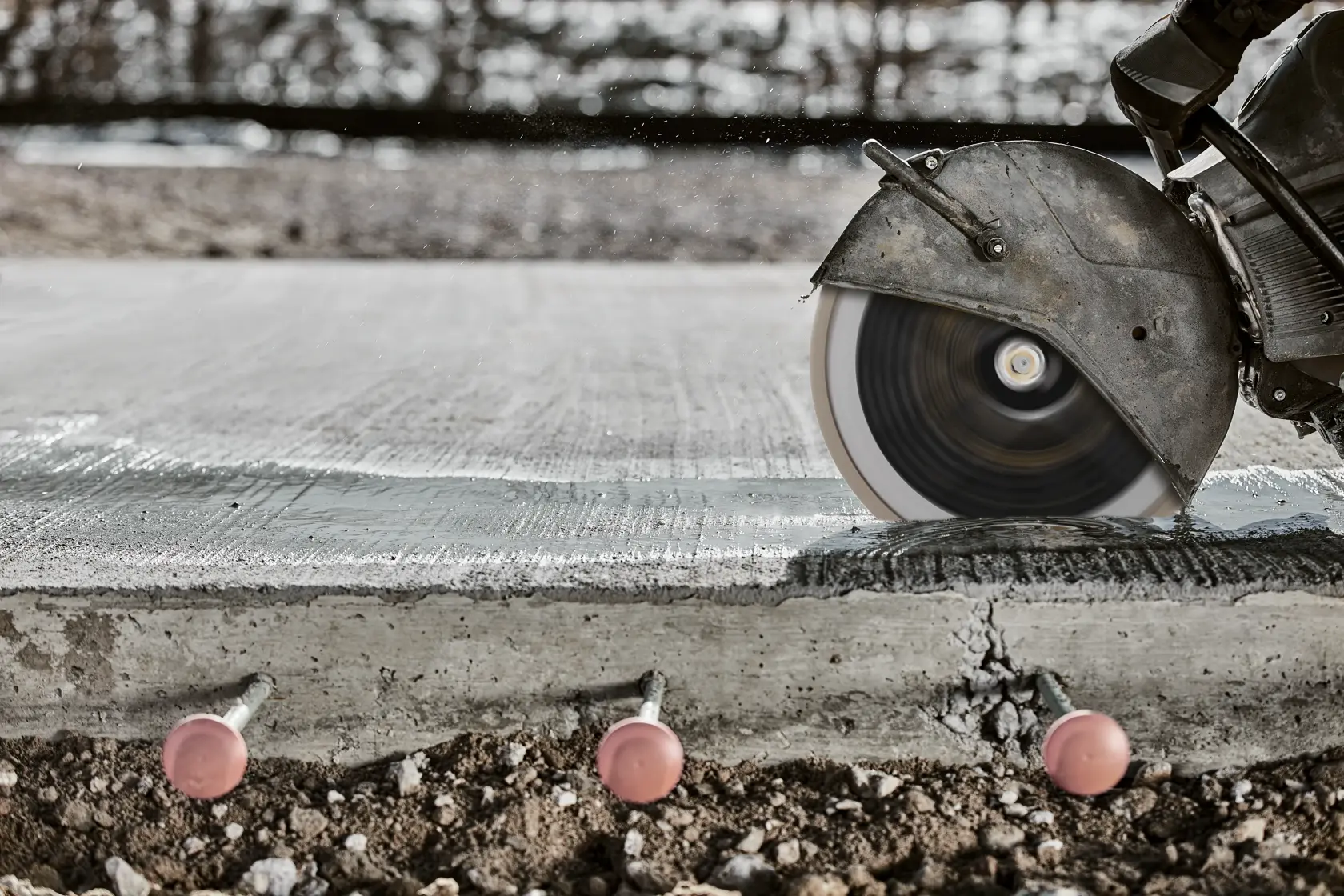 Scie circulaire découpant une dalle en béton, boulons visibles dessous.