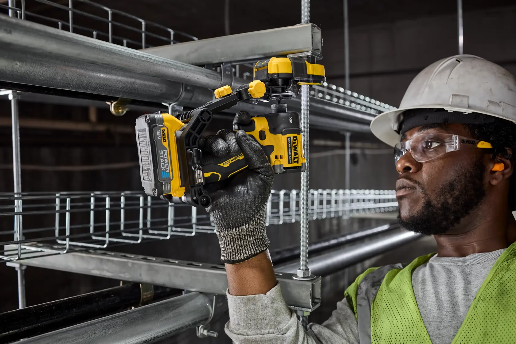 Trabajador usa taladro inalámbrico DEWALT para instalar conducto metálico, lleva guantes, chaleco y casco.