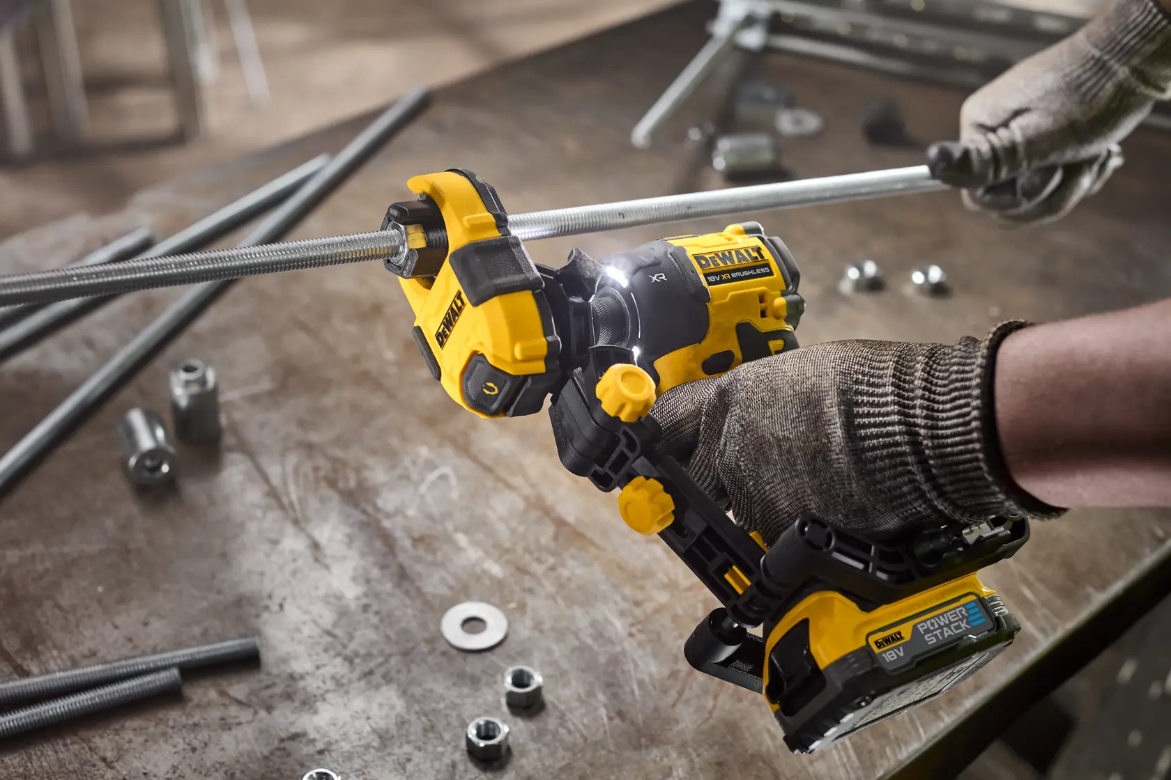 Manos con guantes usan herramienta DEWALT para cortar barra metálica en mesa de taller con tuercas.