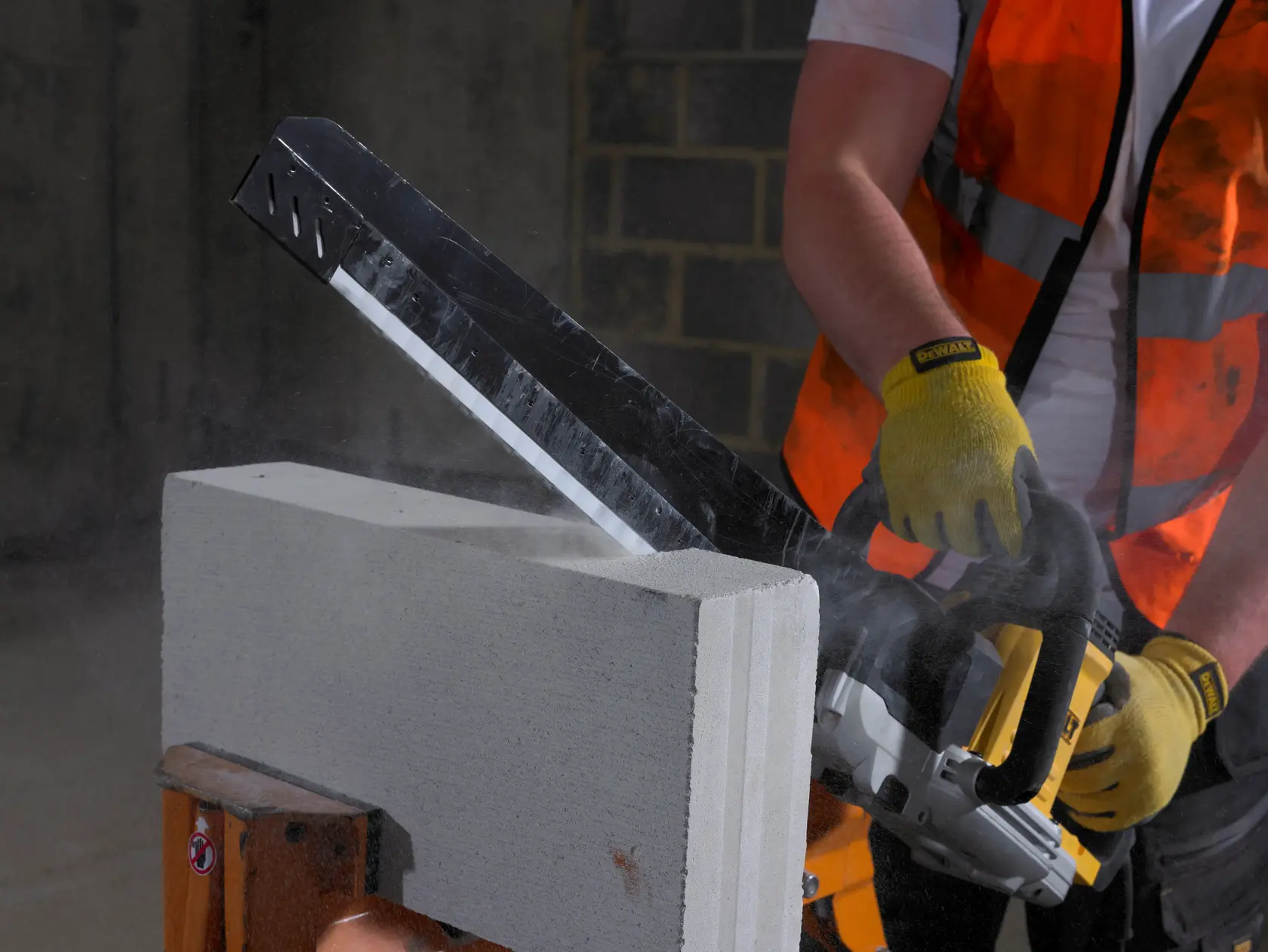 Ouvrier découpe bloc de béton avec une scie DEWALT, gants et gilet de sécurité.