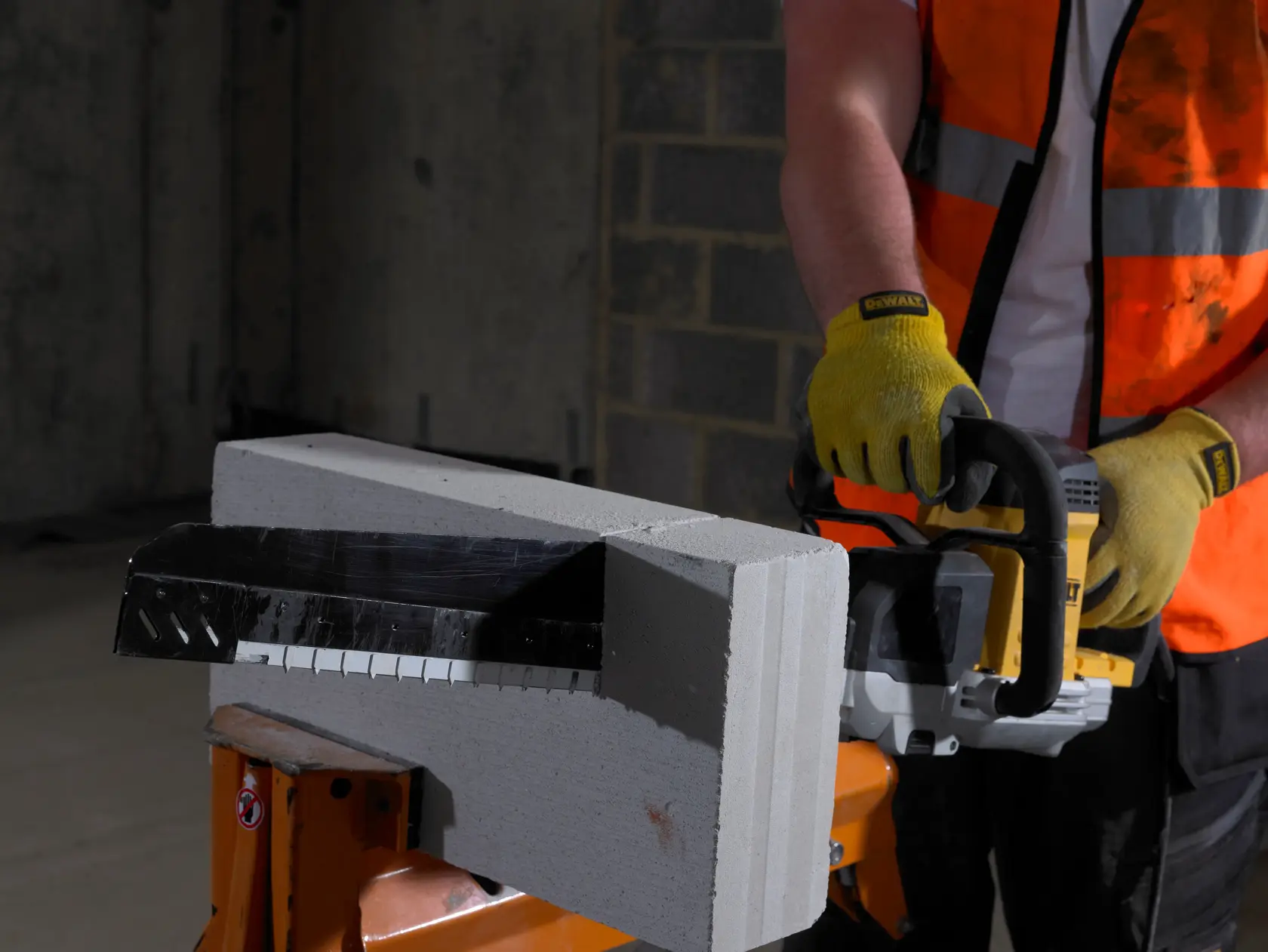 Personne utilise une scie DEWALT avec des gants pour couper un bloc de béton.