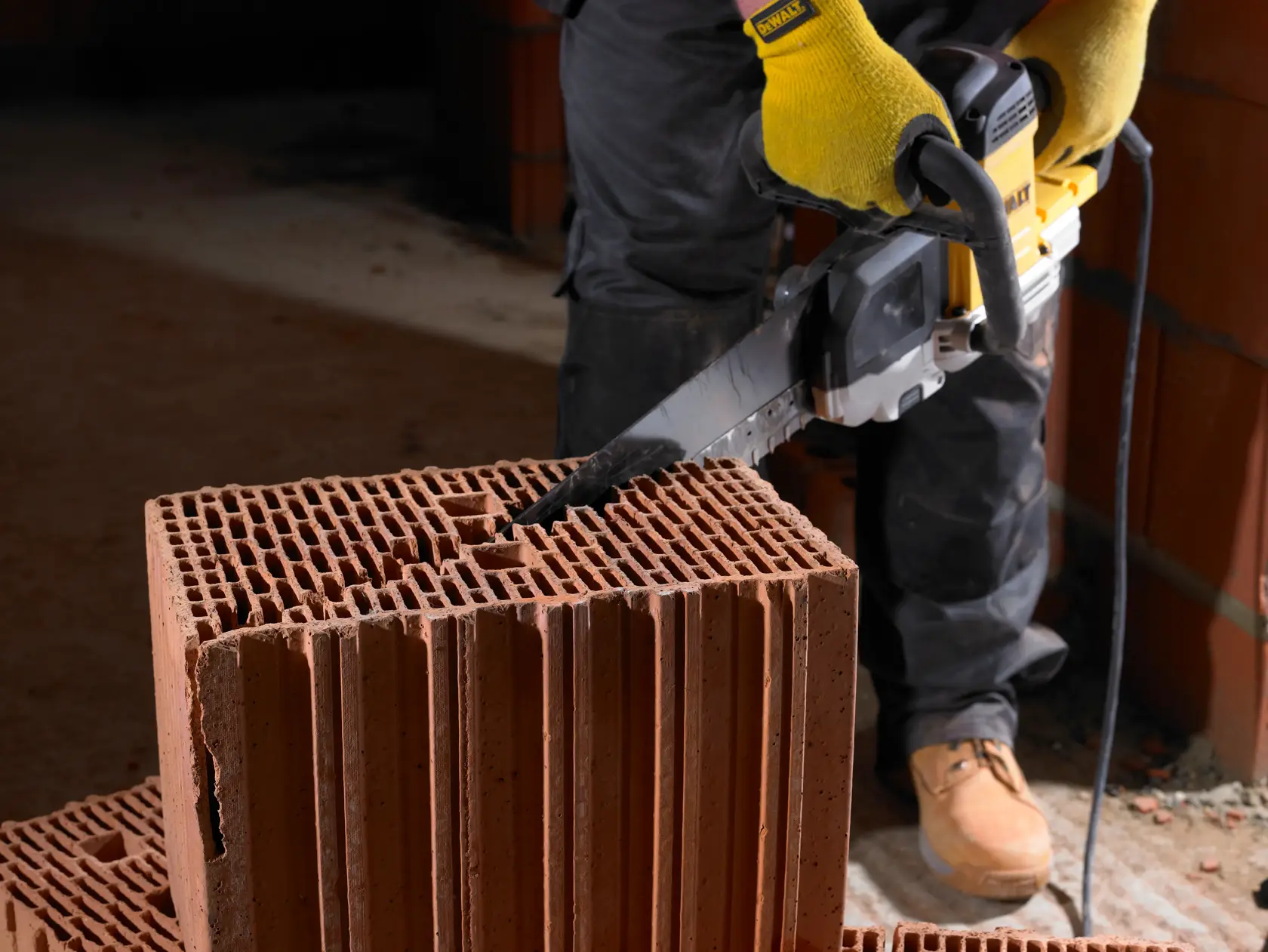 Personne coupe un grand bloc de brique creuse avec une scie électrique DEWALT sur chantier.