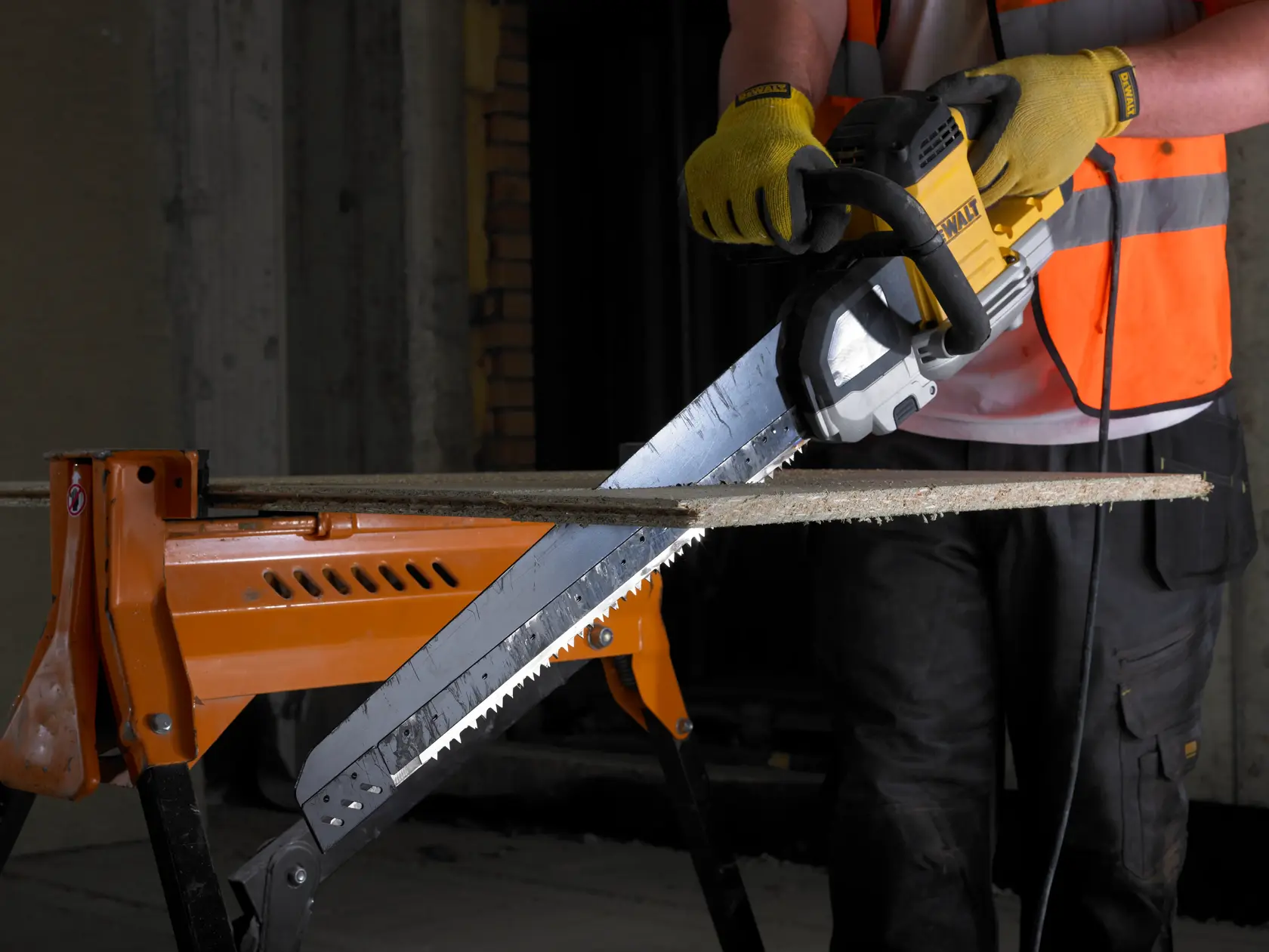 Personne scie du bois avec une scie électrique DEWALT, gants et gilet, bois sur établi orange.