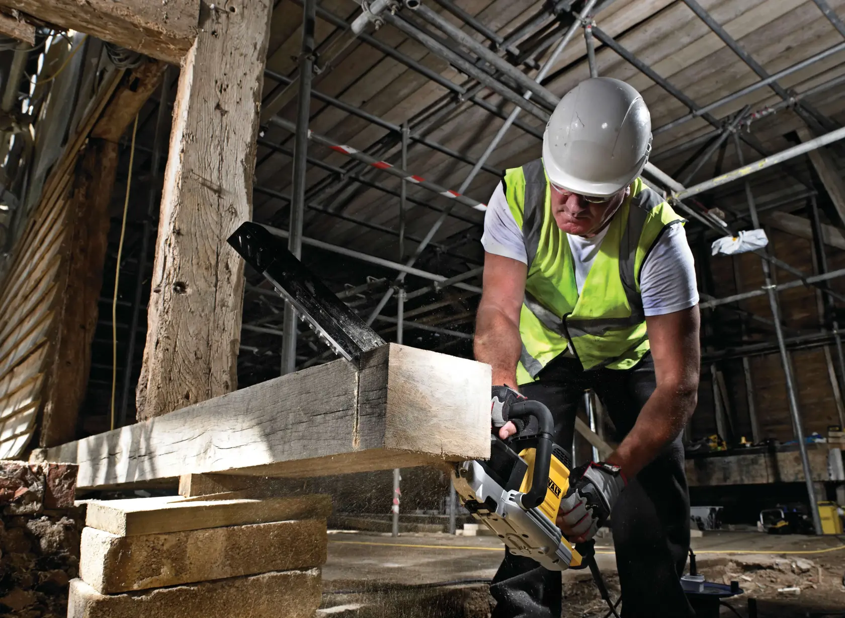 Travailleur équipé utilise une scie DEWALT pour couper une poutre en bois sur un chantier.
