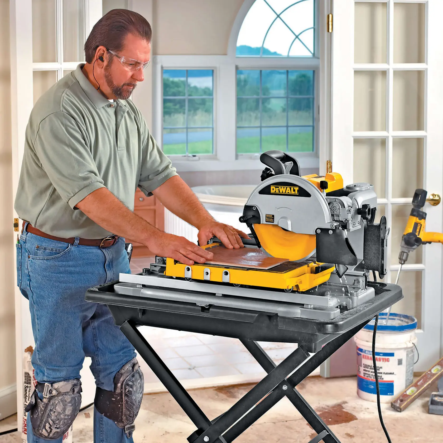 Personne découpe des carreaux en intérieur avec une scie DEWALT DT3733, genouillères et protection auditive.