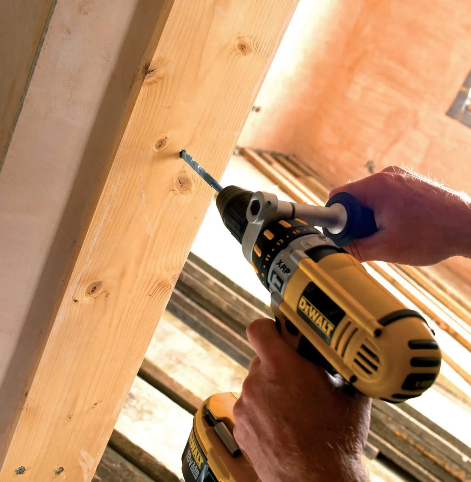 Une personne perce un trou dans une poutre en bois avec une perceuse DEWALT sur un chantier.