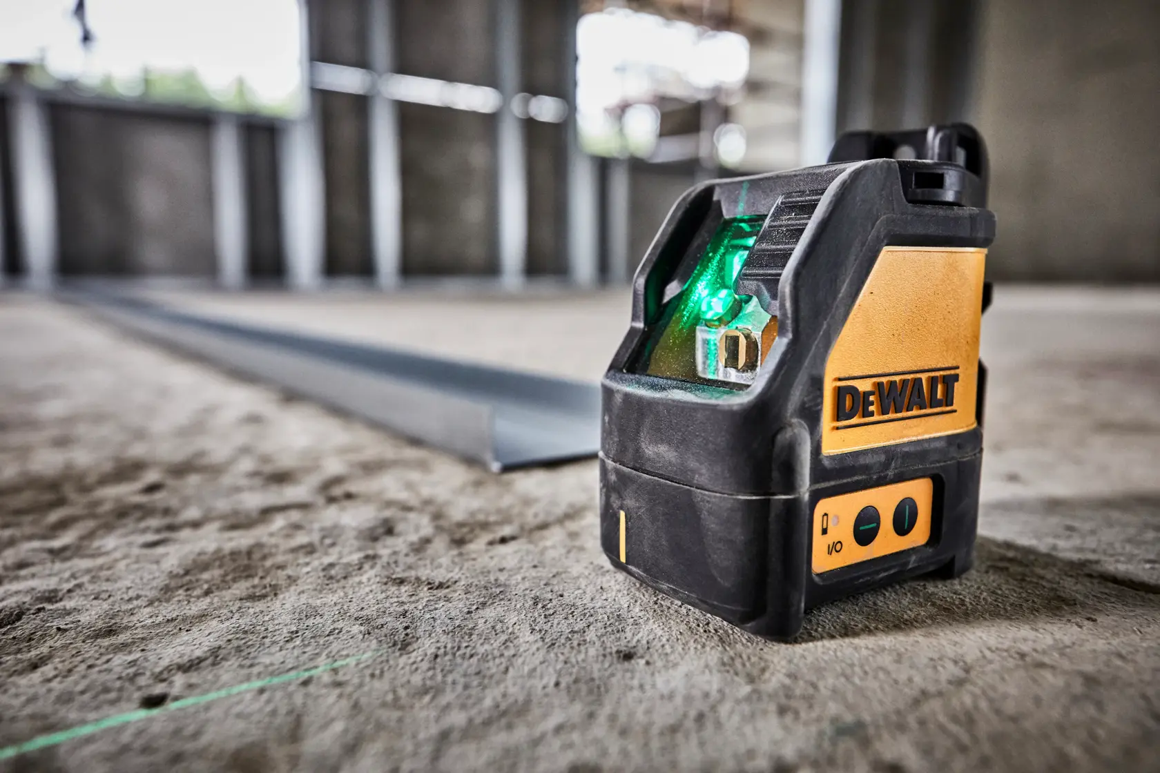 Un niveau laser à ligne croisée verte DEWALT DW088CG placé sur le sol d'un chantier, émettant un faisceau laser vert visible.