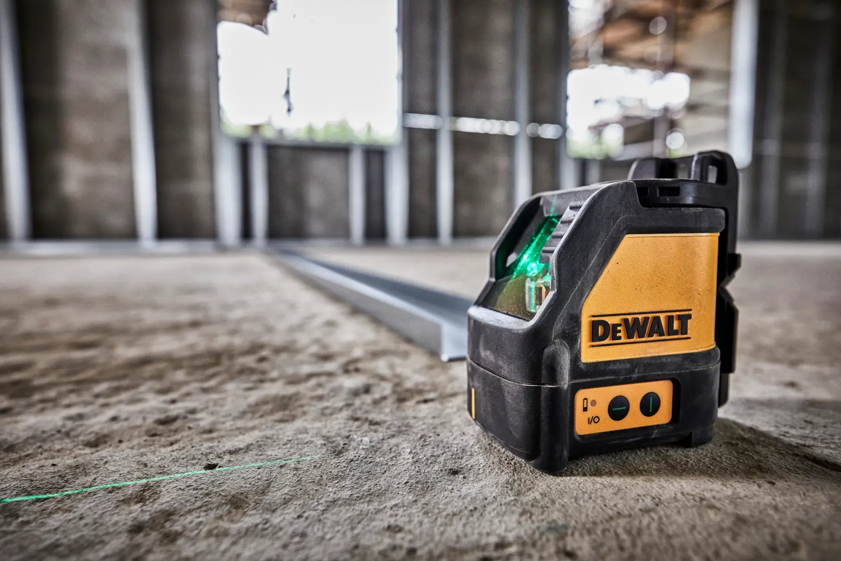 Un niveau laser vert DEWALT DW088CG est placé sur un sol en béton dans un chantier de construction. L'appareil projette une