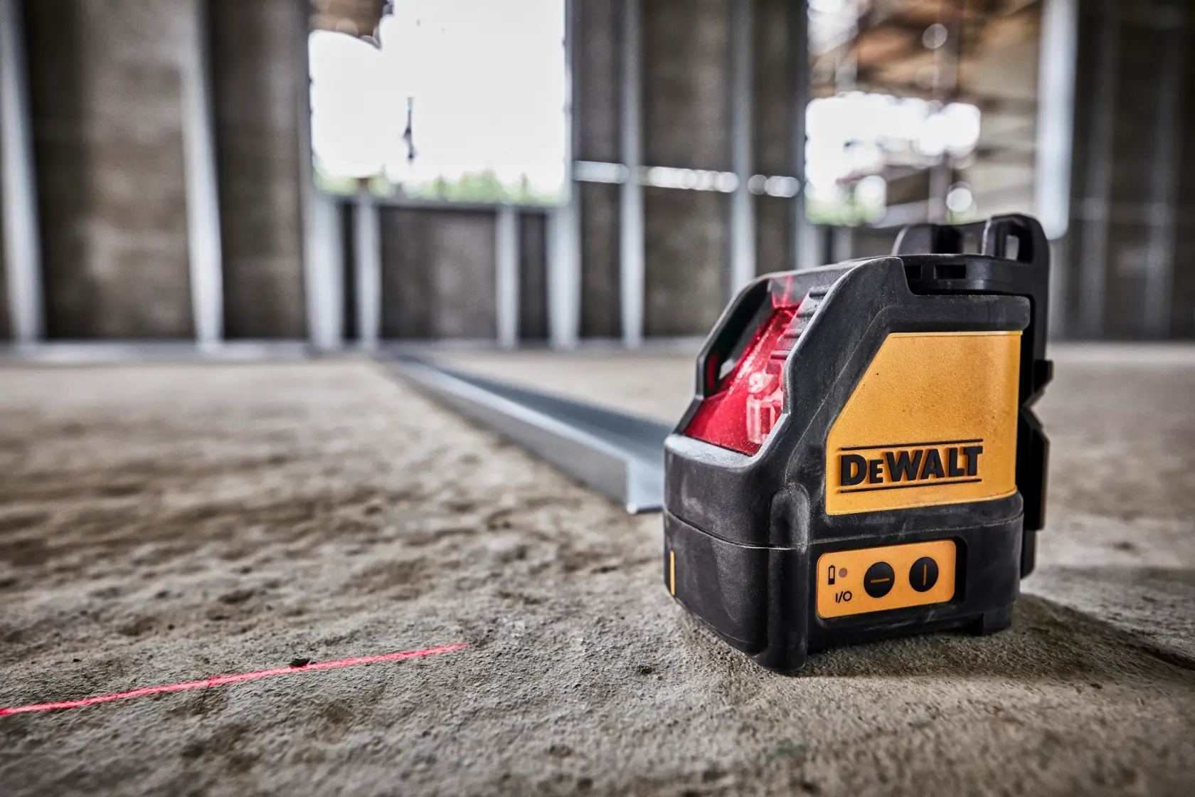 Un niveau laser à lignes croisées auto-nivellant DEWALT DW088K posé sur le sol d’un chantier, projetant une ligne laser rouge visible pour des tâches d’alignement.