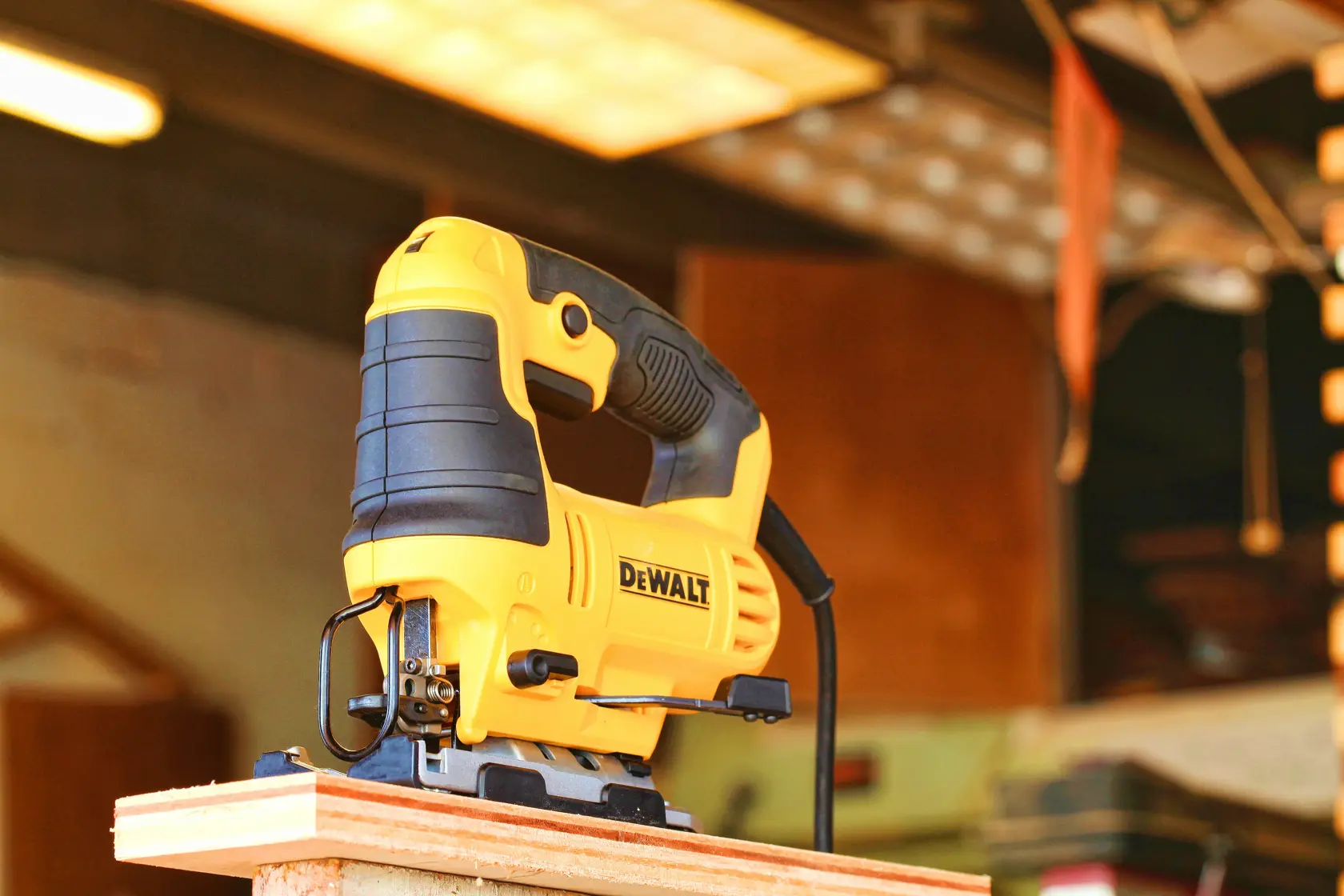 Une scie sauteuse électrique jaune et noire DEWALT est placée sur le bord d'une pièce de bois dans un atelier.