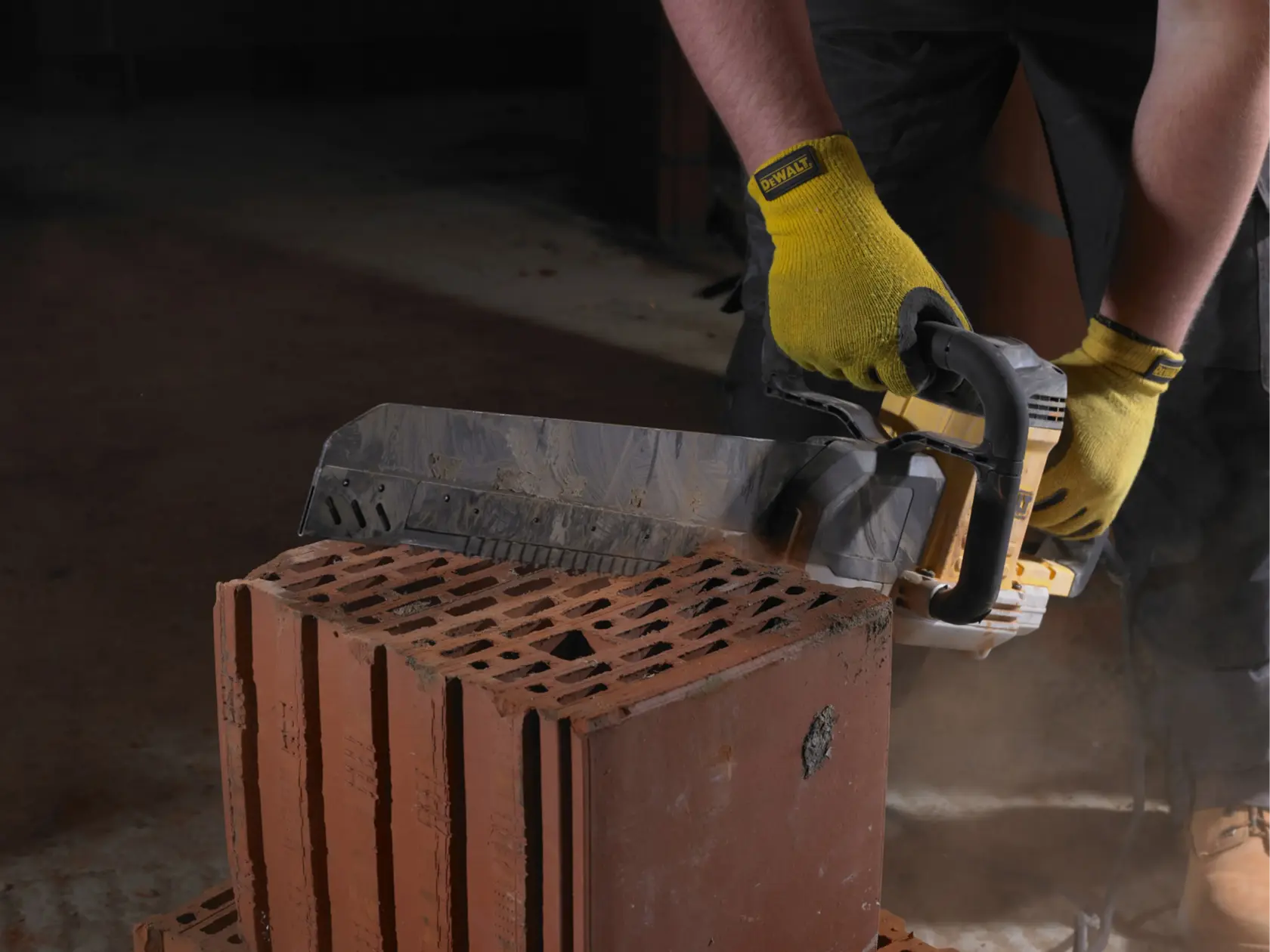 Personne coupe une brique avec une scie DEWALT, portant des gants jaunes, sur un chantier.