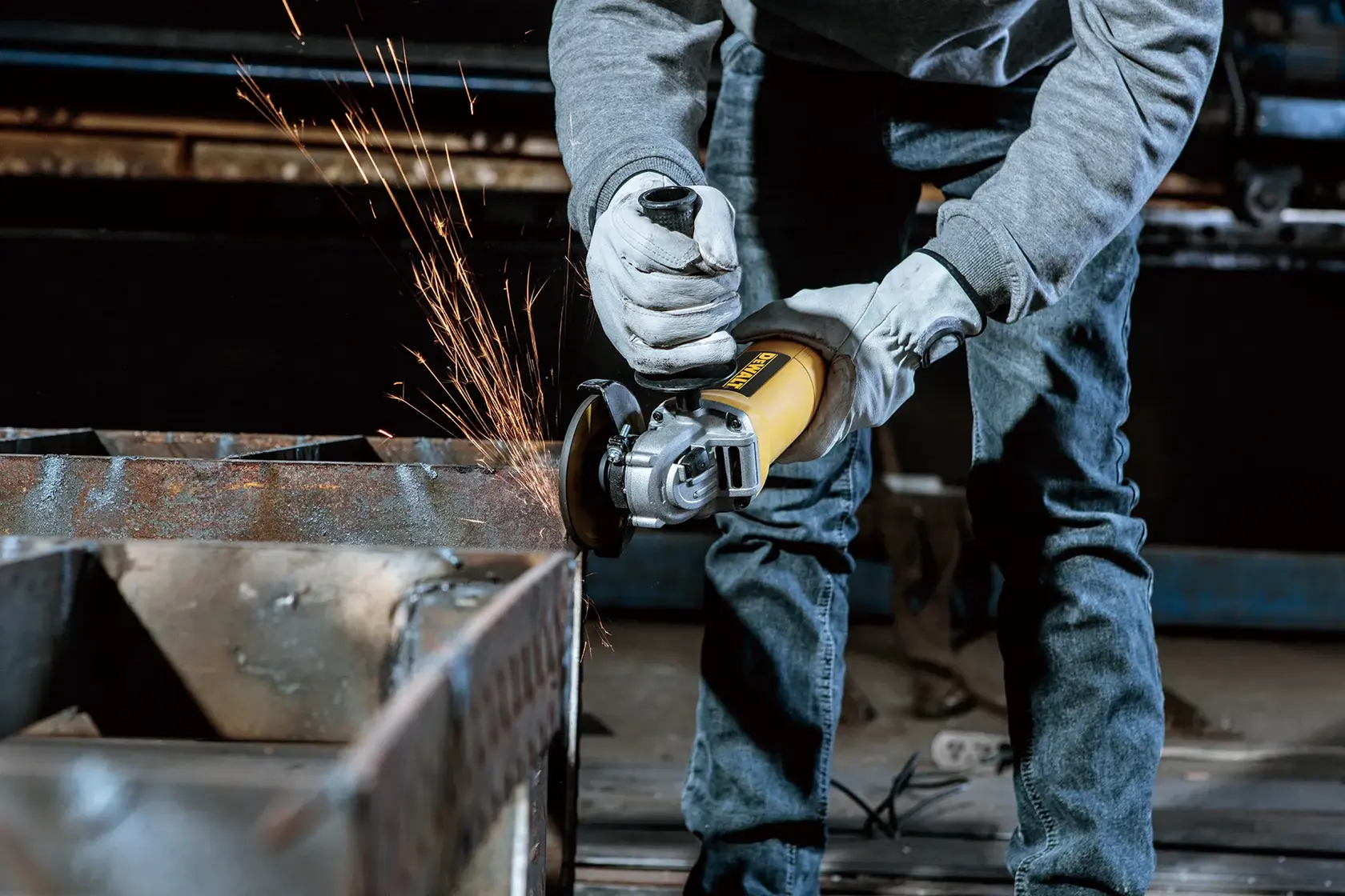 Une personne portant des gants utilise une meuleuse angulaire jaune DEWALT pour poncer une surface métallique, produisant des étincelles.