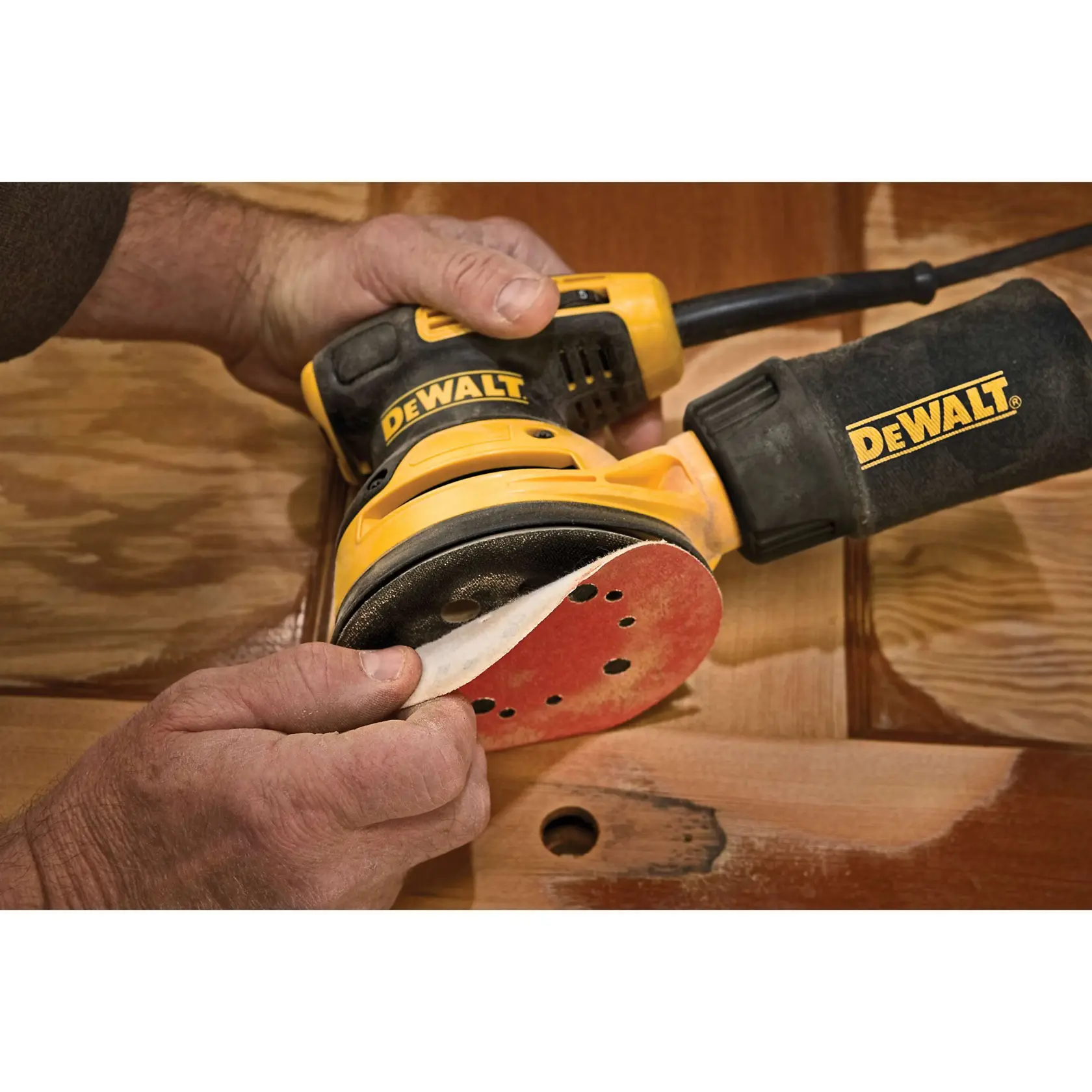 Ponceuse orbitale électrique DEWALT avec sac à poussière, au design jaune et noir. Texte en dessous : 'Contrôle stable avec poignée recouverte de caoutchouc.'