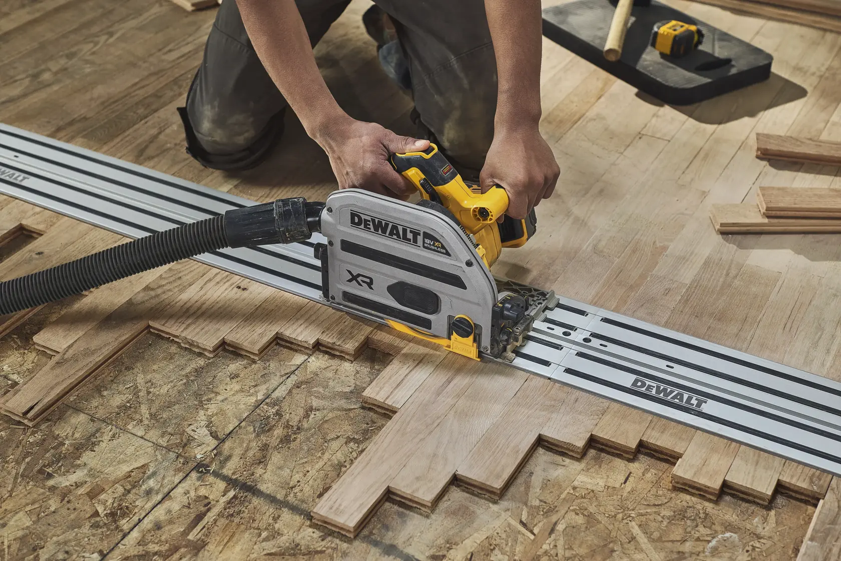 Une personne coupe un parquet en bois avec une scie sur rail DEWALT pour des coupes précises.