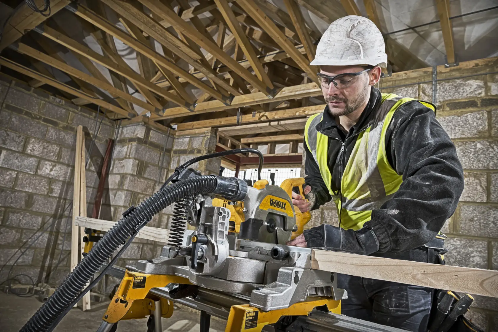 Ouvrier coupe du bois avec DEWALT DWS777 sur chantier. Équipement de sécurité et gilet réfléchissant.